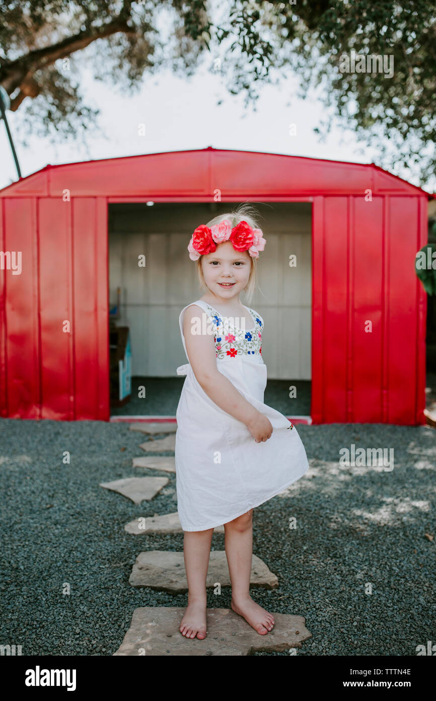 Portrait of cute girl wearing tiara standing on footpath against red garage in yard Stock Photo