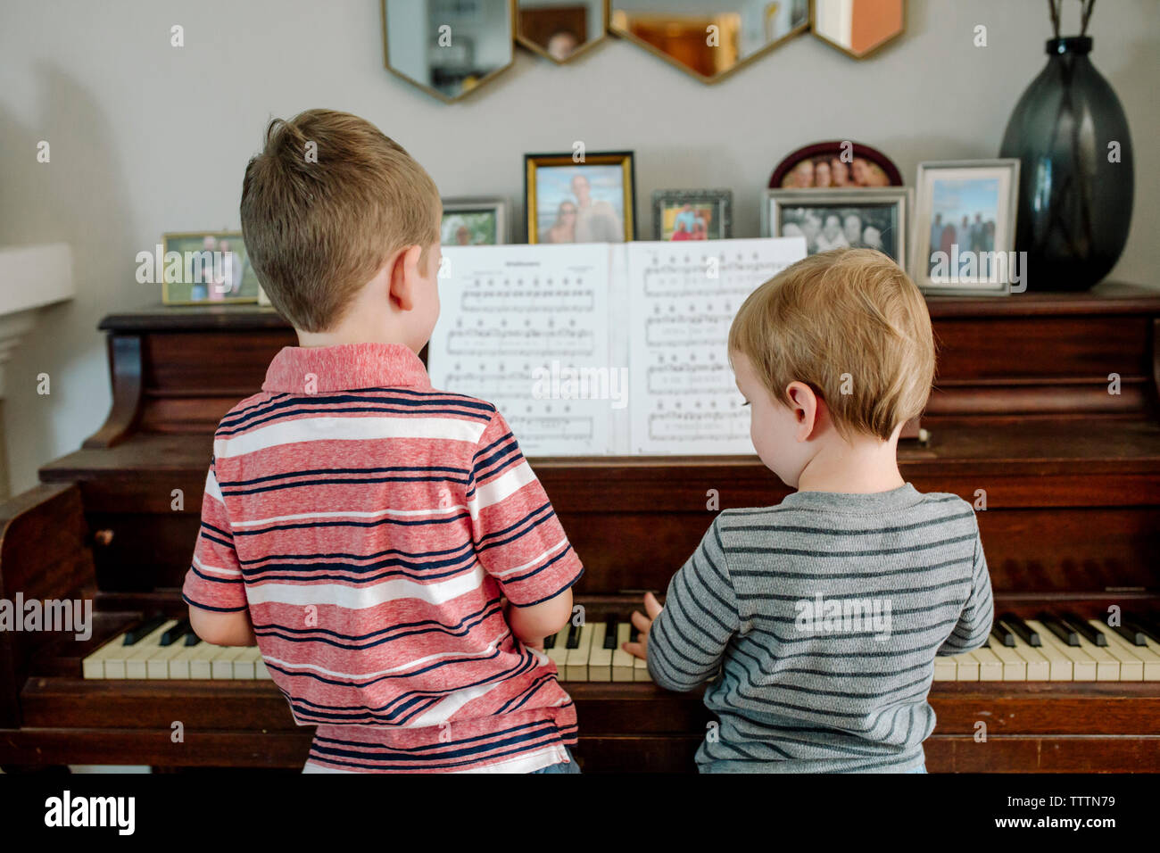 Rear view of brothers playing piano together at home Stock Photo