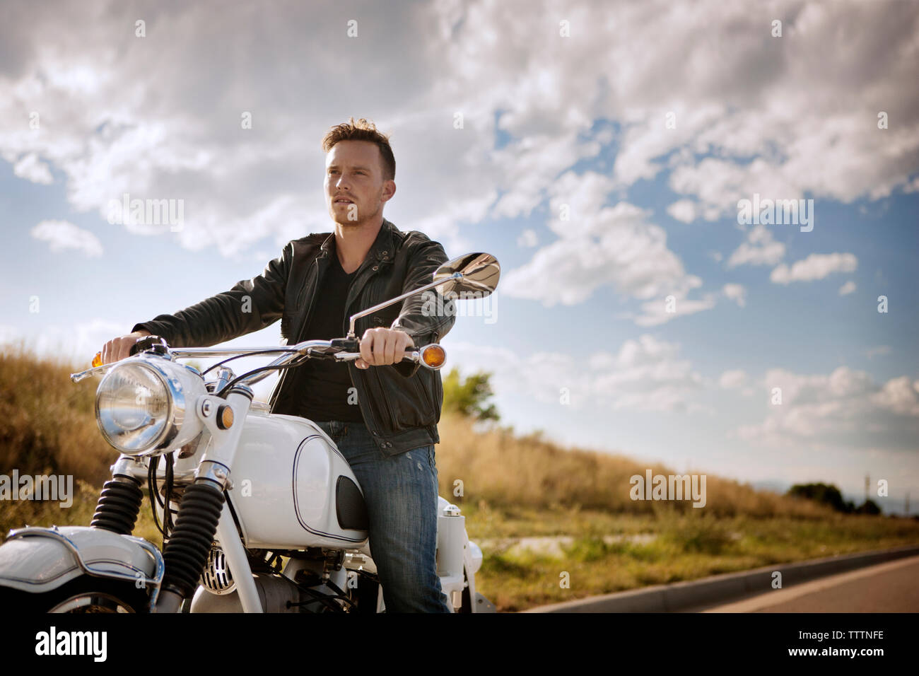 Biker riding motorcycle against cloudy sky Stock Photo