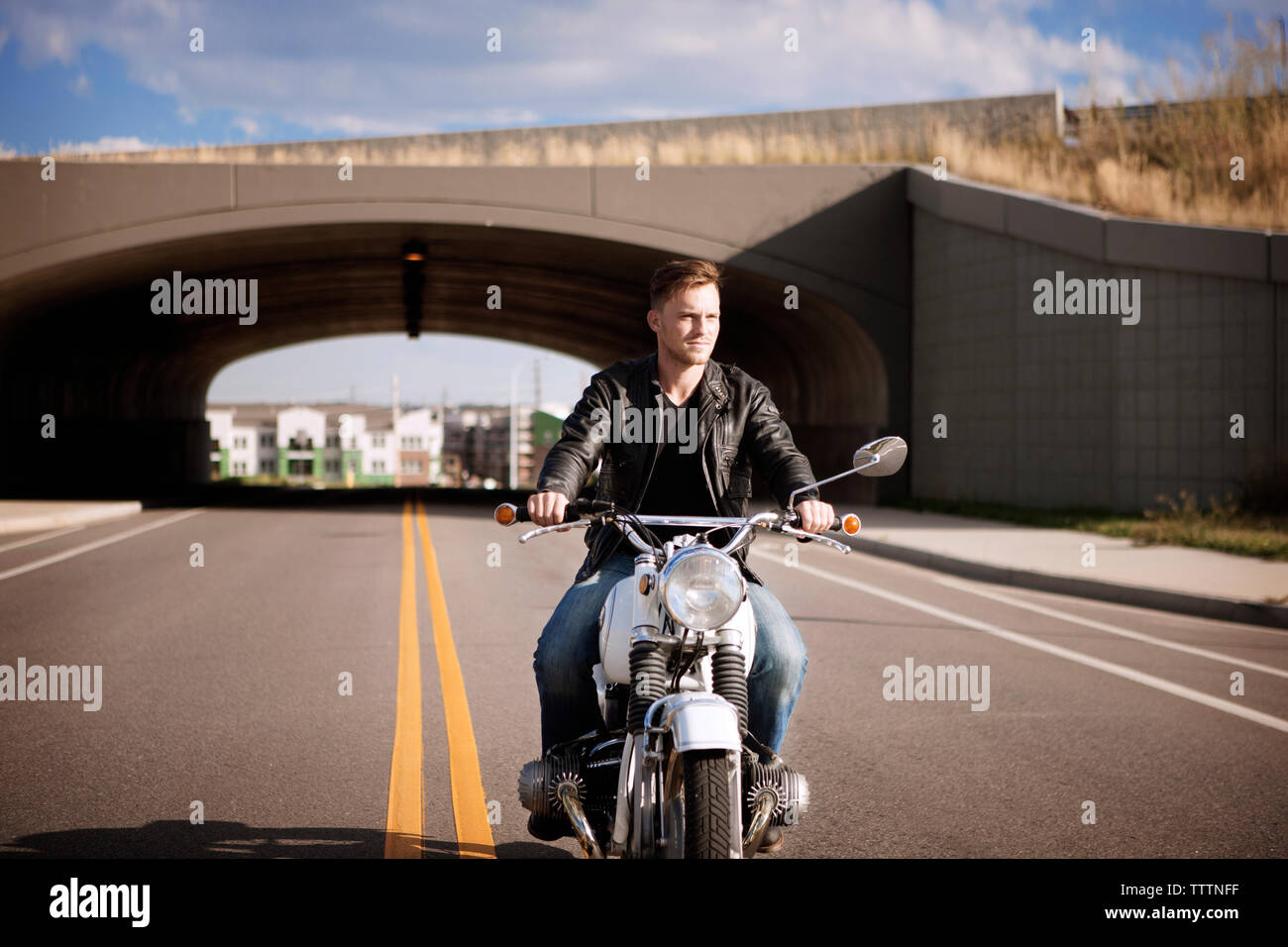 Biker riding motorcycle with bridge in background Stock Photo