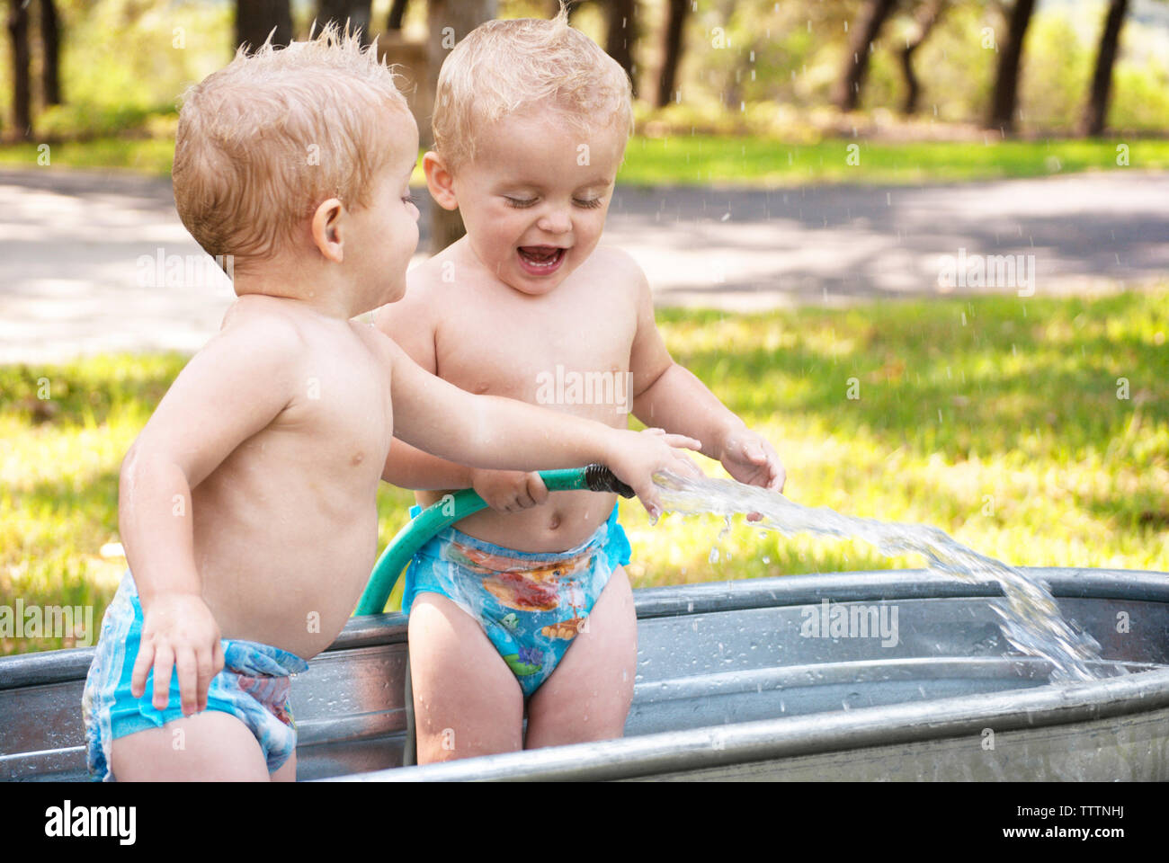 Cheerful twin baby girls playing with water in washtub Stock Photo