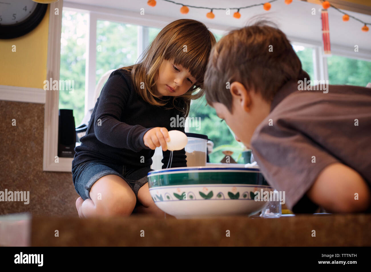 Sibling breaking egg into bowl in kitchen Stock Photo