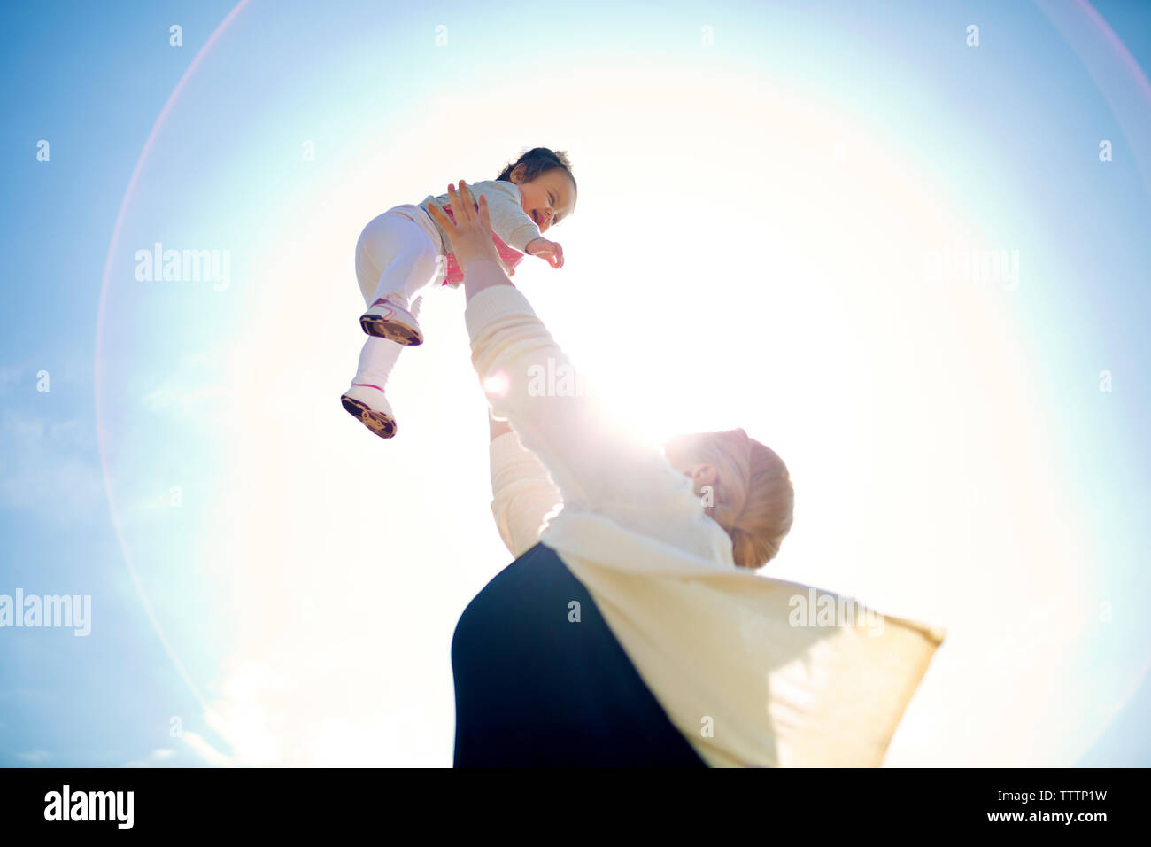 Low angle view of woman lifting baby against sky Stock Photo