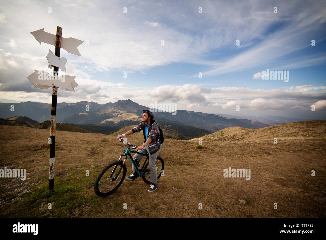 Cyclist on bicycle looking at sign board against cloudy sky Stock Photo