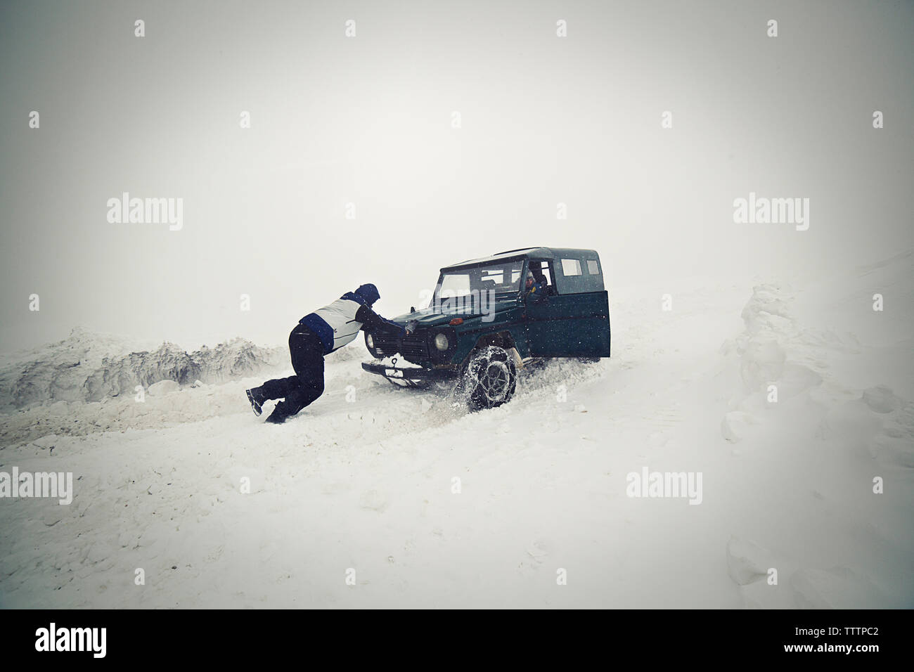 Man pushing car on snow field Stock Photo