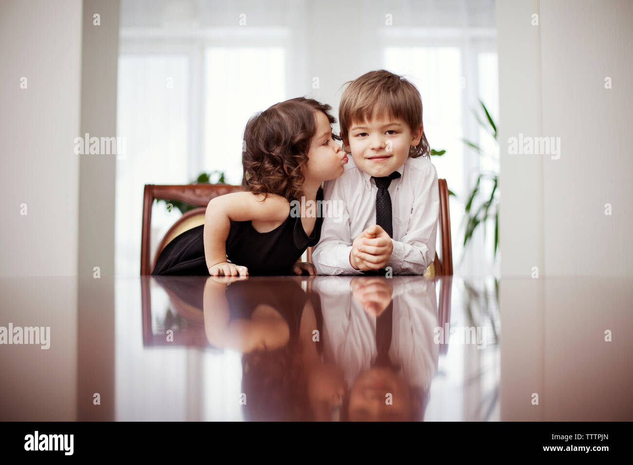 Cute girl kissing brother while sitting at table Stock Photo