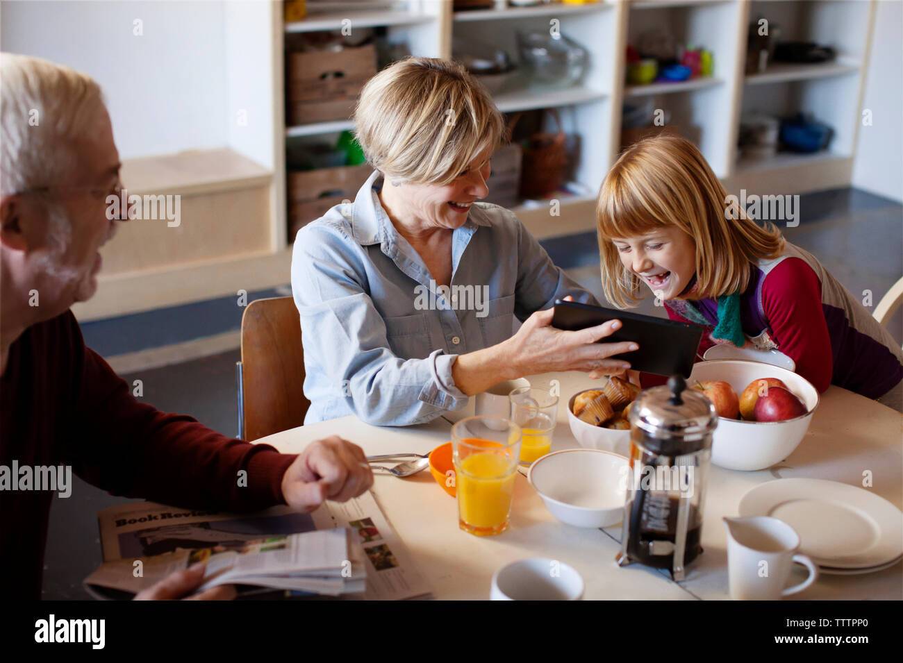 Man looking at wife showing tablet computer to granddaughter while sitting at table Stock Photo