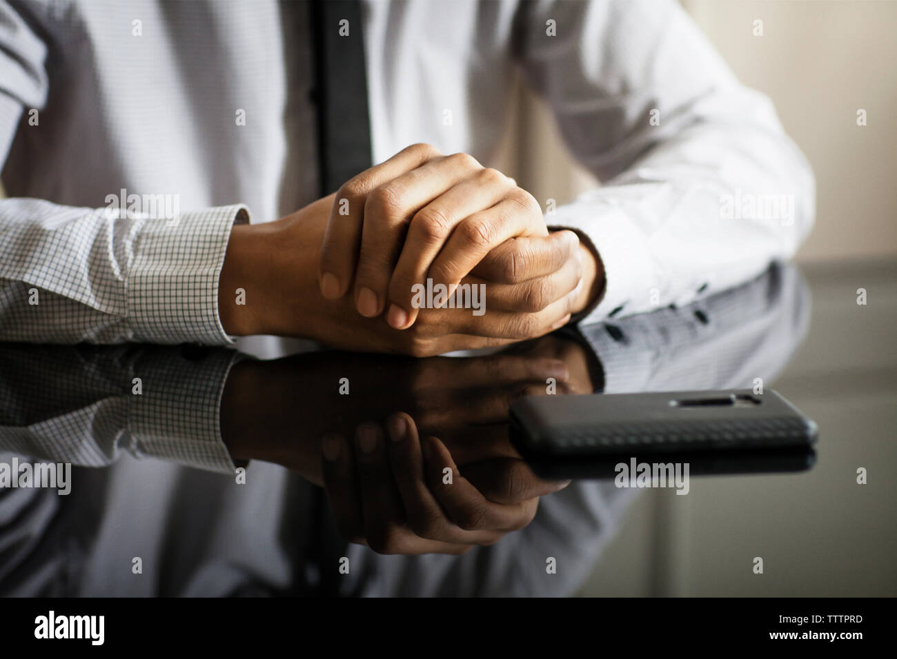 Midsection of businessman with hands clasped sitting at table in office Stock Photo