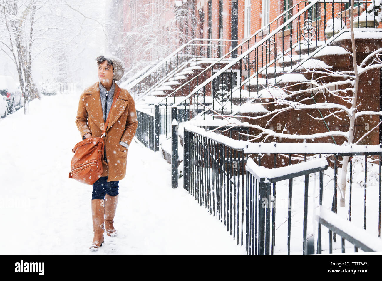 Woman looking away while walking on snow covered field during snowing Stock Photo