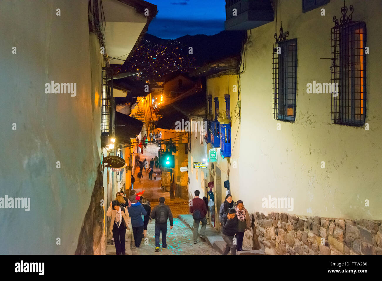 People walking on cobblestone street lined up with colonial houses at night, Cusco, Peru Stock Photo