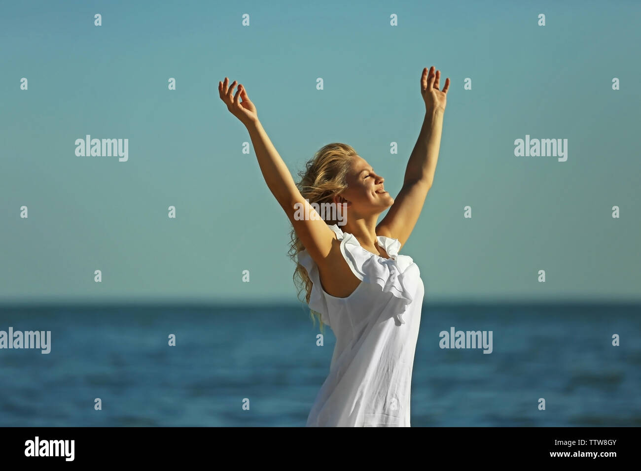 Young woman with raising hands on blue sky background Stock Photo - Alamy