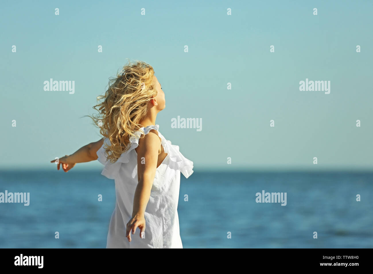 Young woman with raising hands on blue sky background Stock Photo - Alamy