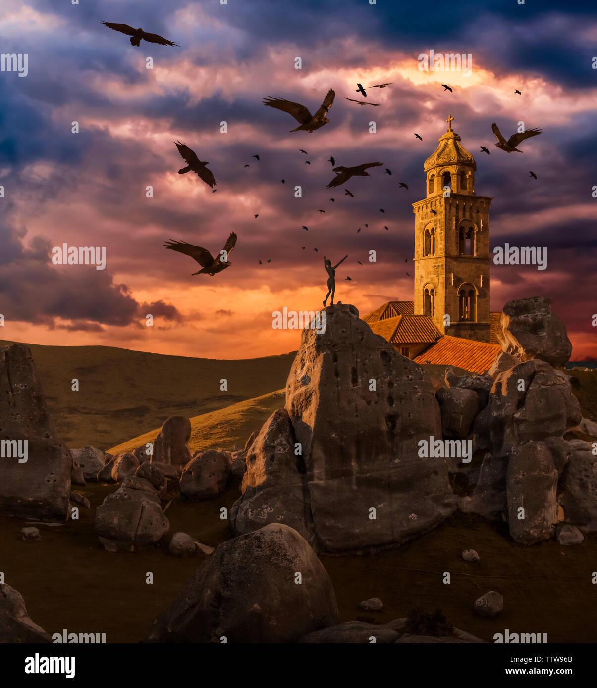 Crows flying towards a church tower with a wooden human mannequin laying on the ground in the foreground Stock Photo