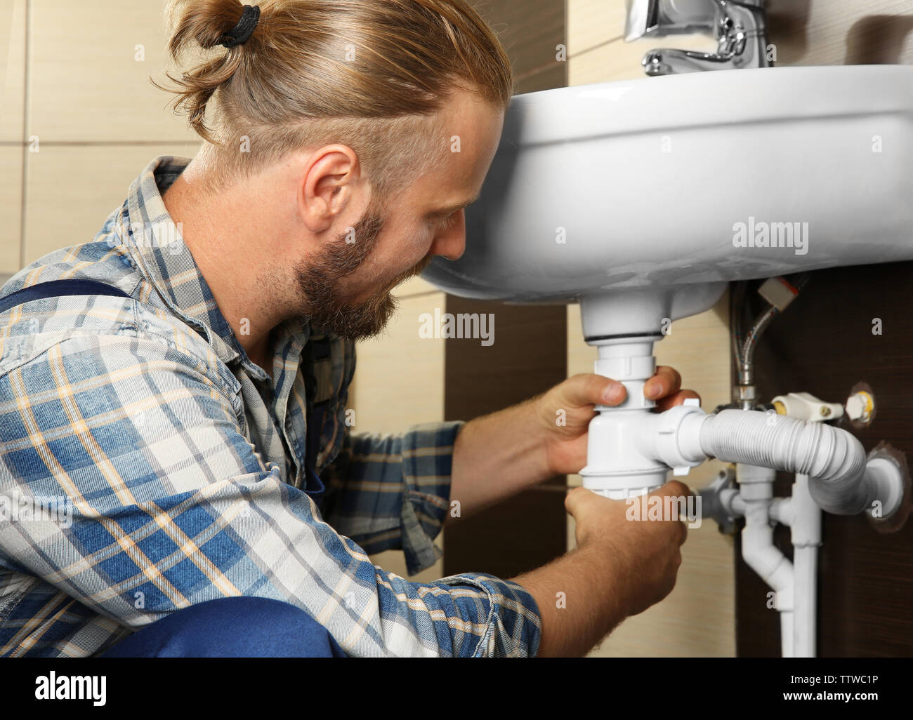 Handsome plumber assembling sink pipes in bathroom, close up view Stock Photo