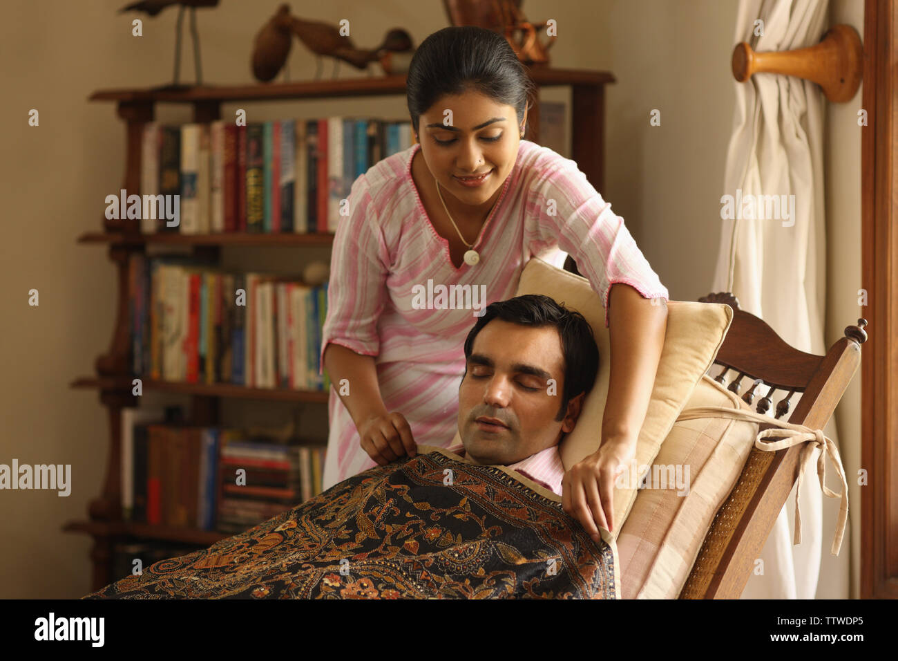 Woman putting blanket over her husband sleeping on reclining chair