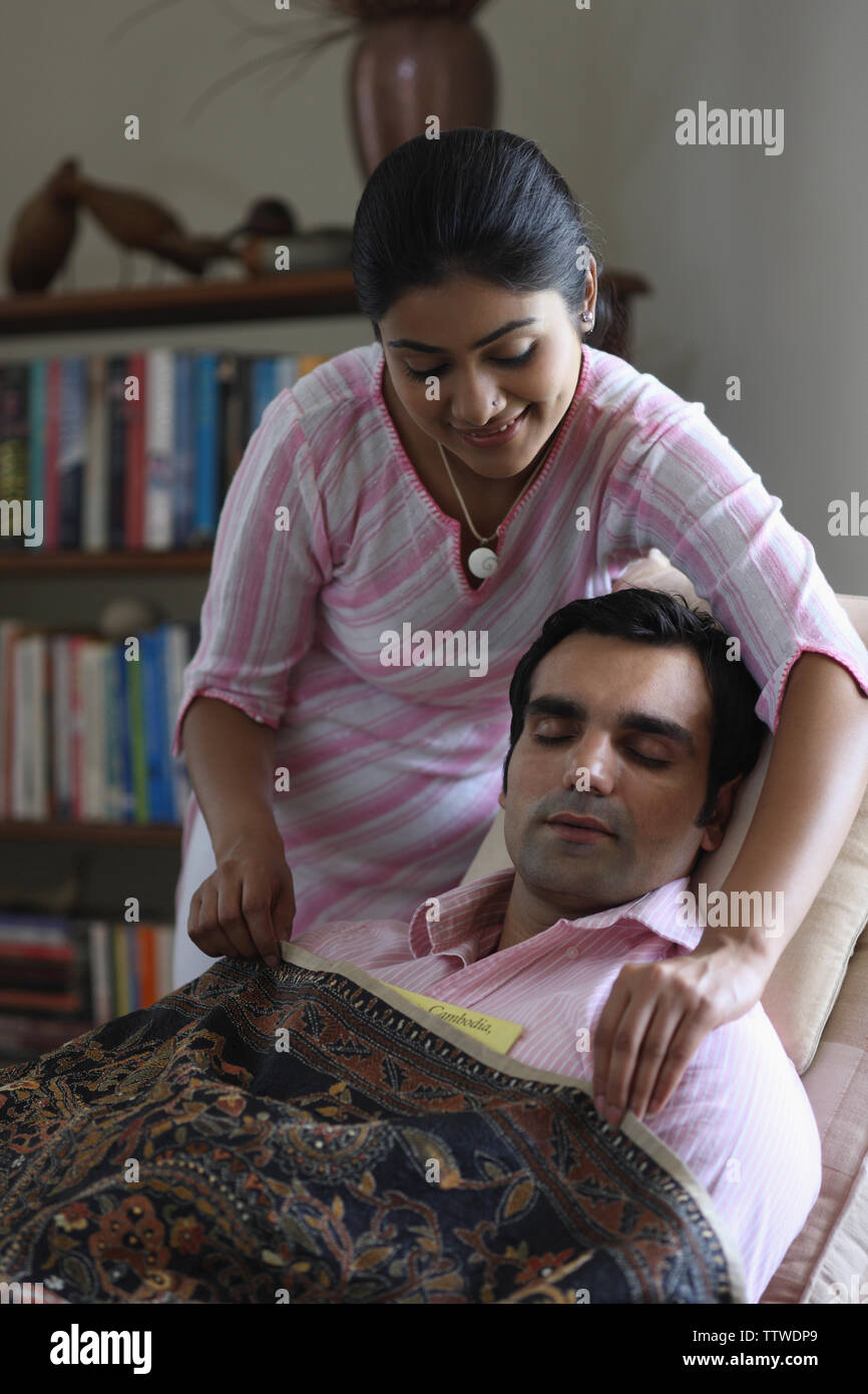 Indian woman putting blanket over her husband sleeping on reclining