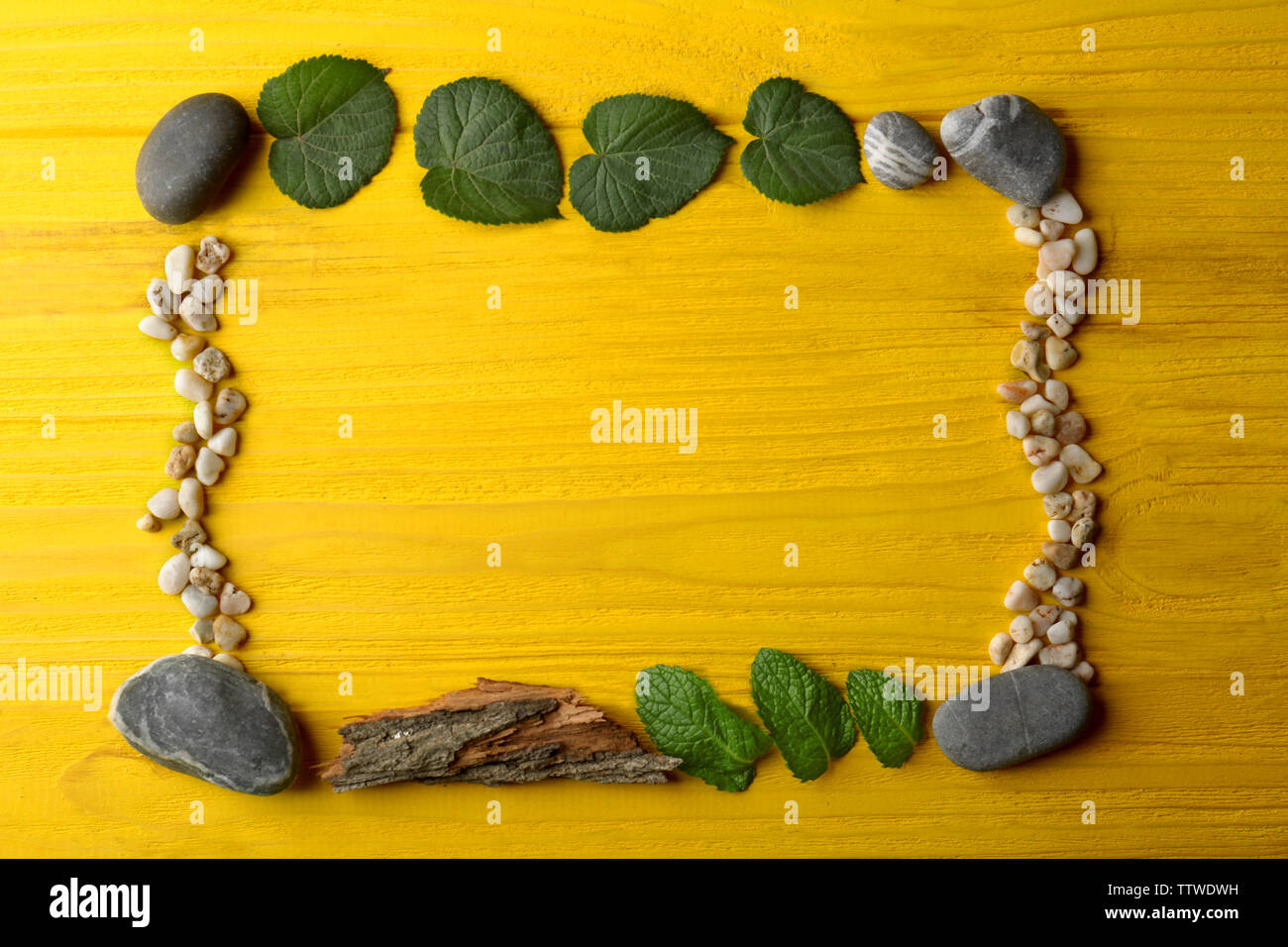 Rectangular frame made of pebbles, leaves and bark on yellow wooden background Stock Photo