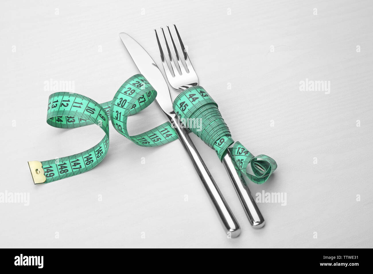 Measuring tape wrapped around knife and fork lying on white table. Diet