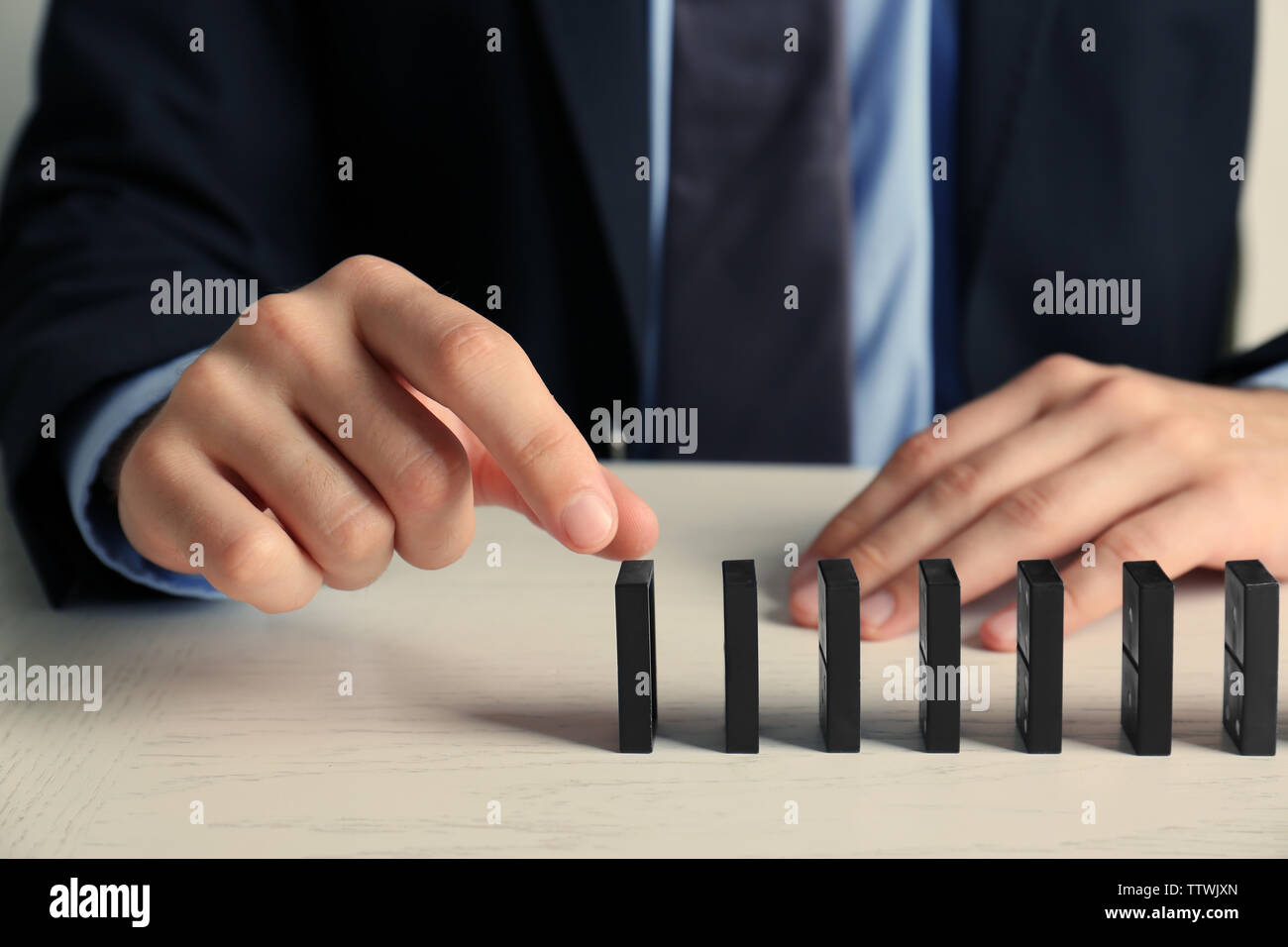 Businessman hand trying to toppling dominoes on table Stock Photo