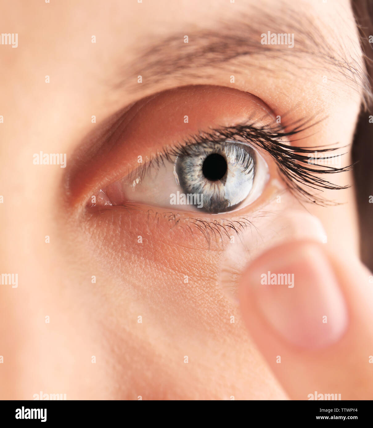 Close up view of young woman putting contact lens in her eye Stock Photo