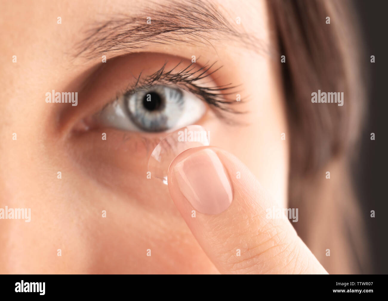 Close up view of young woman putting contact lens in her eye Stock Photo