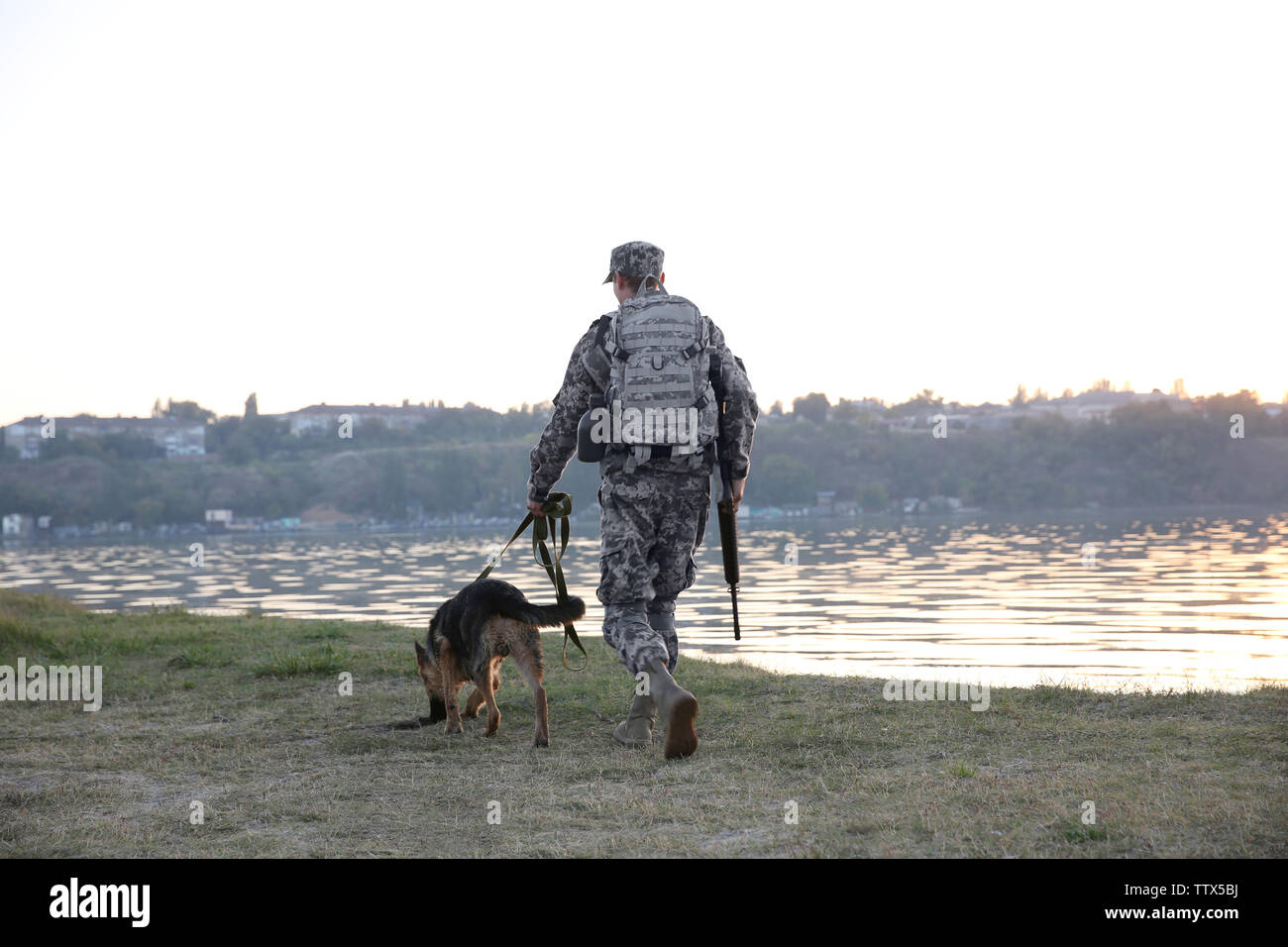 Soldier with german shepherd dog near river at sunset Stock Photo