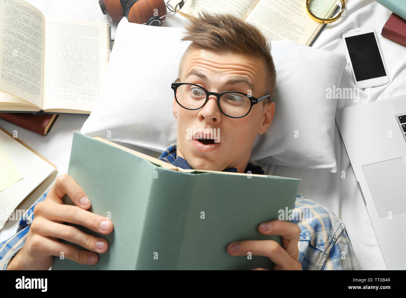 Funny young man reading book while lying on bed Stock Photo - Alamy