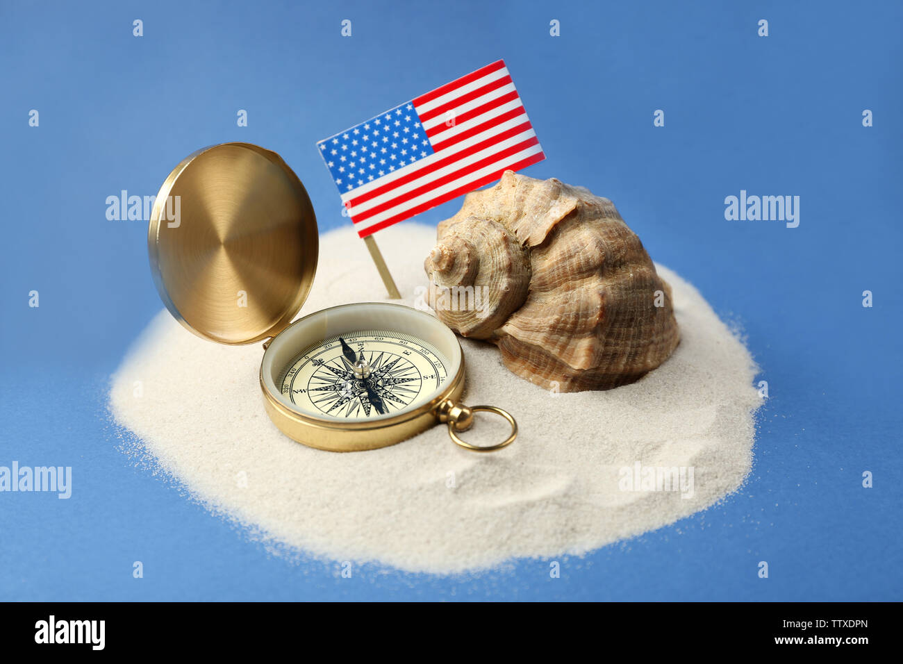 USA flag, compass and shell in sand on blue background. Columbus Day ...