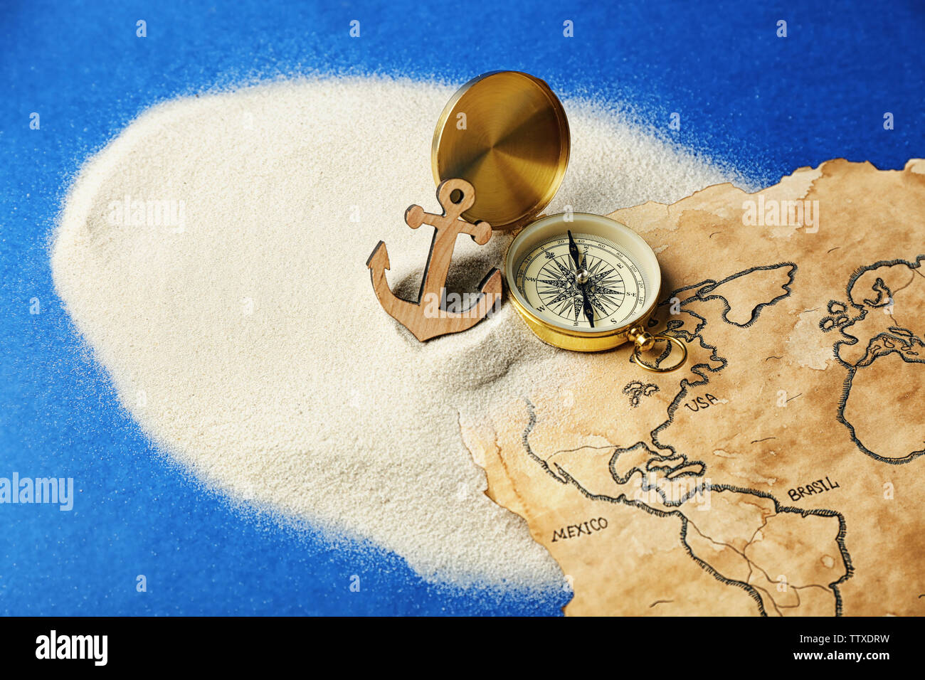 Compass, anchor and old map in sand on blue background. Columbus Day  concept Stock Photo - Alamy
