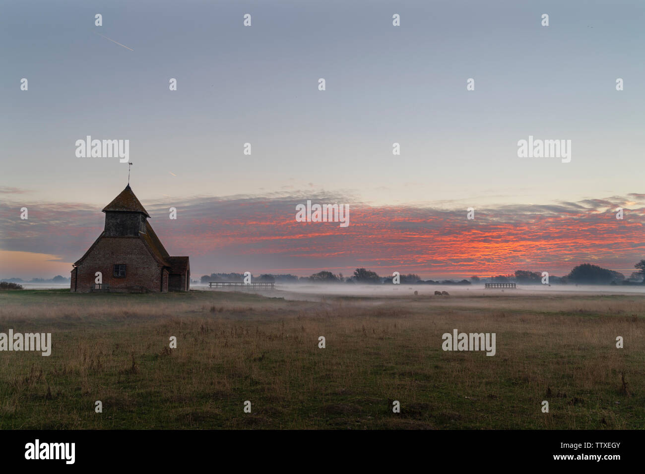 St Thomas Becket church at Romney Marsh. The Church on the marsh at dawn. Ground mist covered, clouds on horizon catching colour from the unrisen sun. Stock Photo