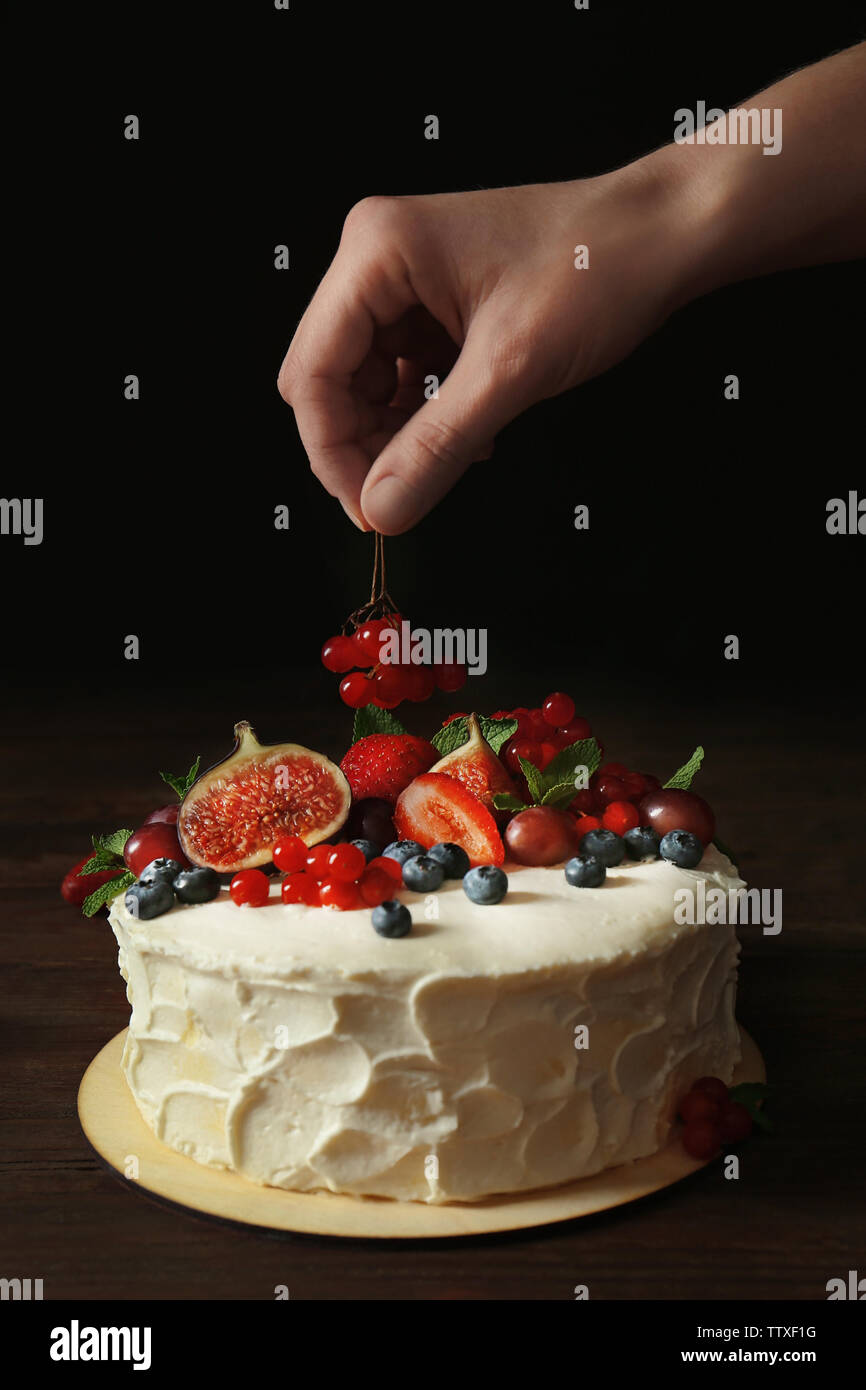 Baker hand decorating creamy cake on table Stock Photo