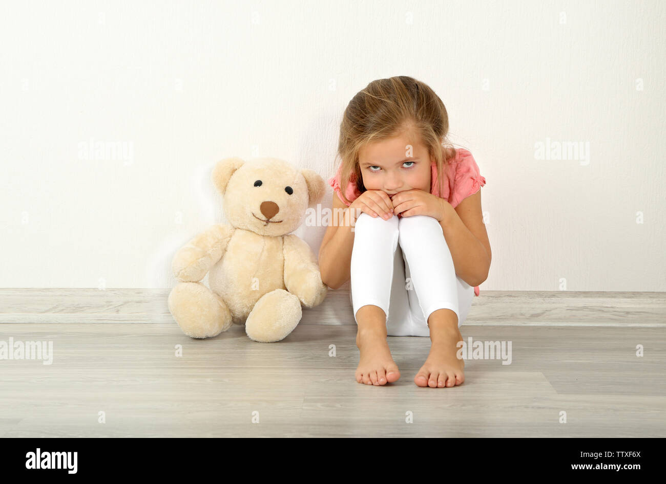 Sad little girl with teddy bear sitting on floor in empty room Stock ...