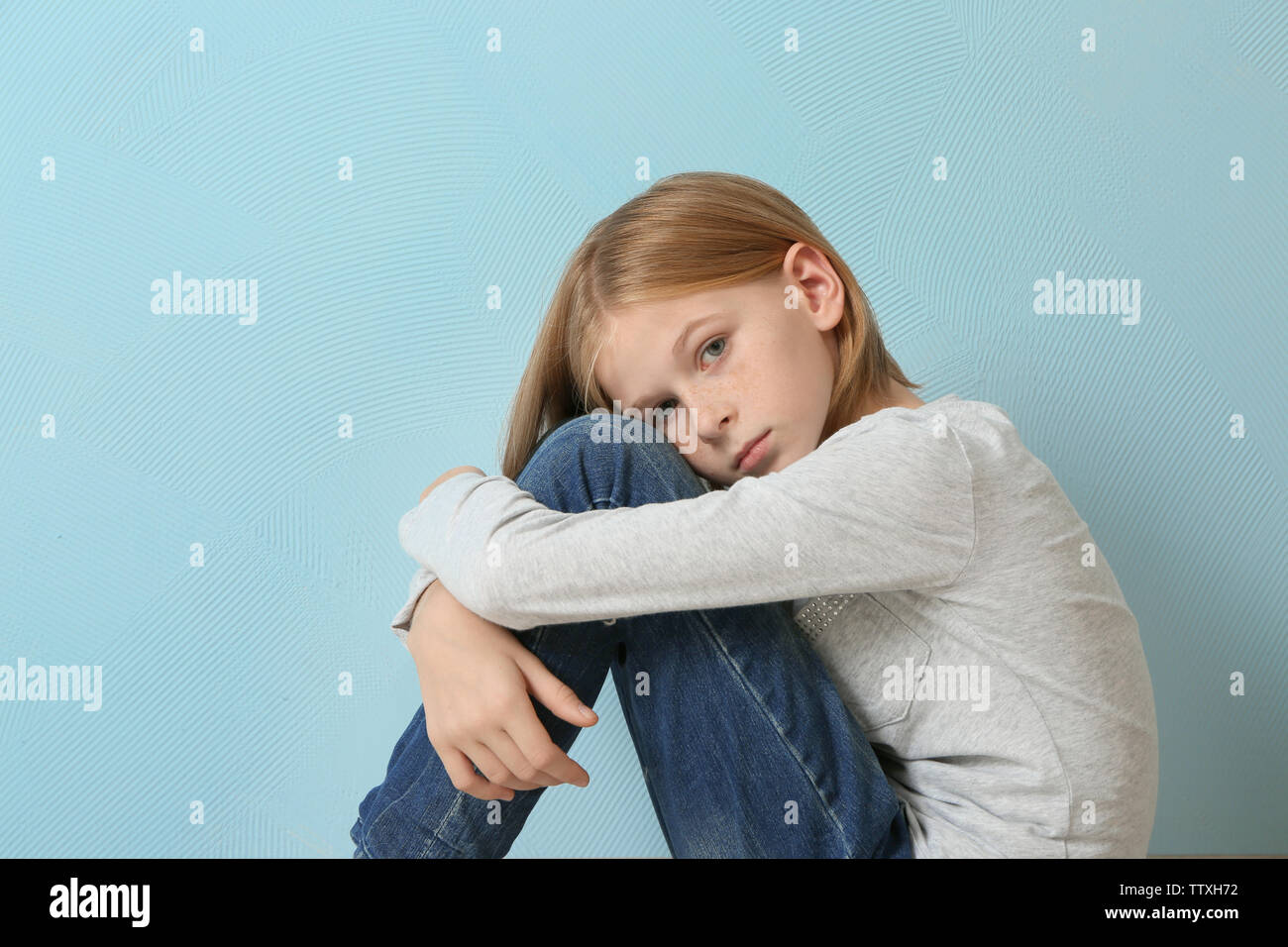 Upset girl sitting on blue wall background Stock Photo - Alamy