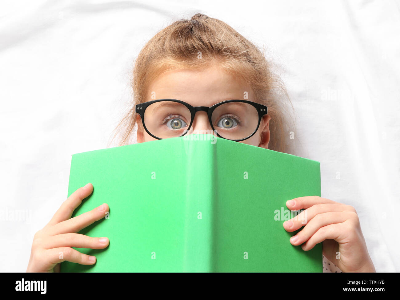 Cute girl with book lying on white sheets Stock Photo - Alamy
