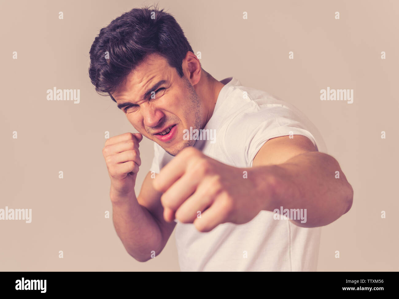 Young attractive man in rage looking furious in defence stance and threaten punching with fist in angry upset and mad face expression isolated grey ba Stock Photo