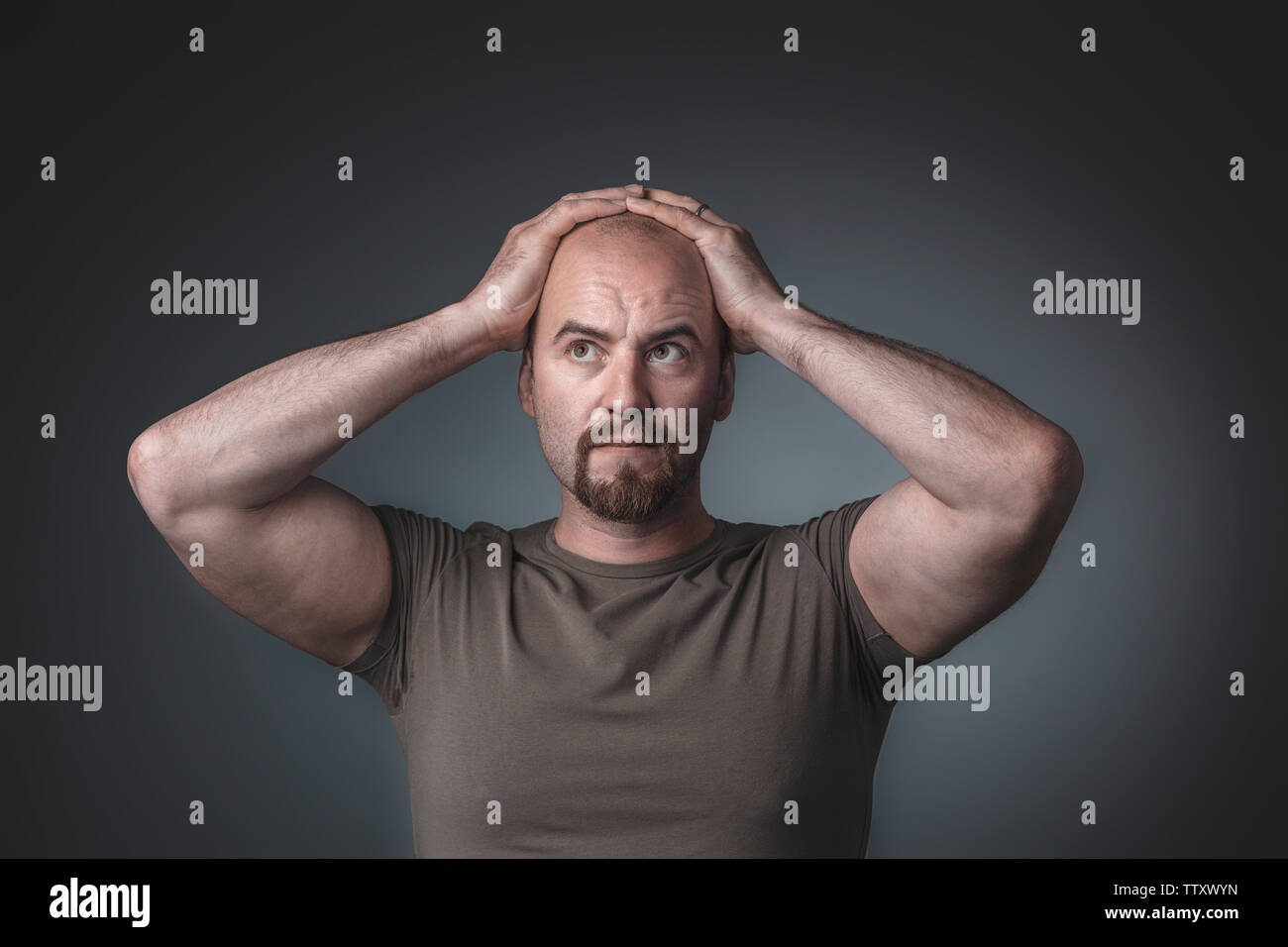 Studio portrait of a man with hands on his head. Expression of stress and indecision, thoughtful. Stock Photo