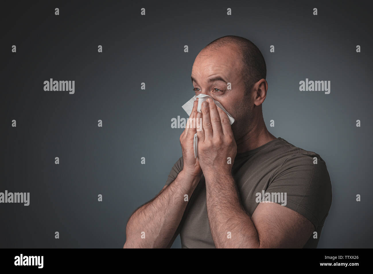 Portrait of a man blowing his nose with a tissue. Concept of health and malaise caused by physical discomfort. Stock Photo