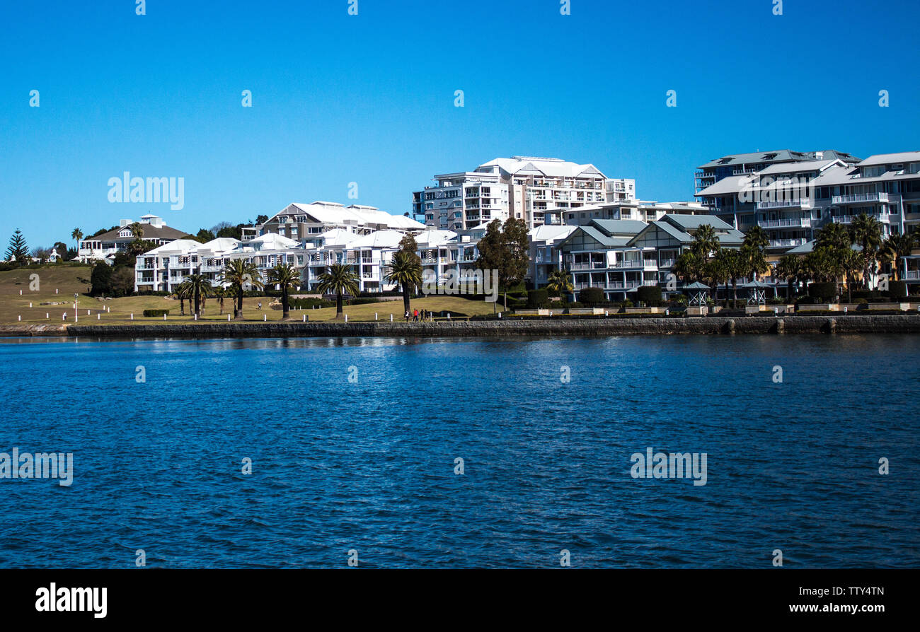Harbourside condominium apartment housing with grass frontage, blue river against blue sky Stock Photo