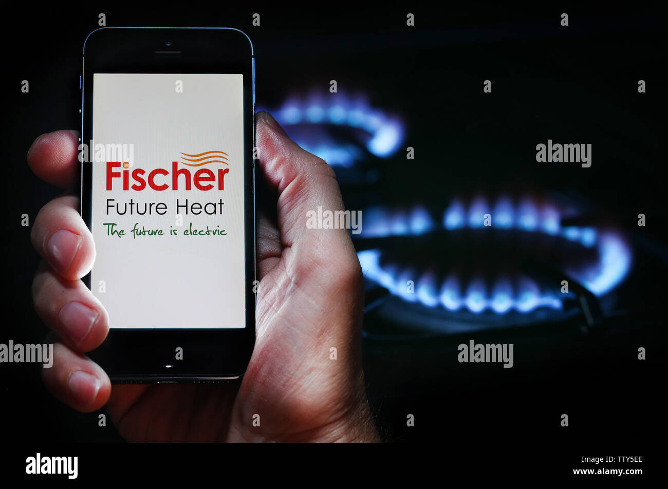 A man looking at the website logo for energy company Fischer on his phone in front of his gas cooker (editorial use only) Stock Photo