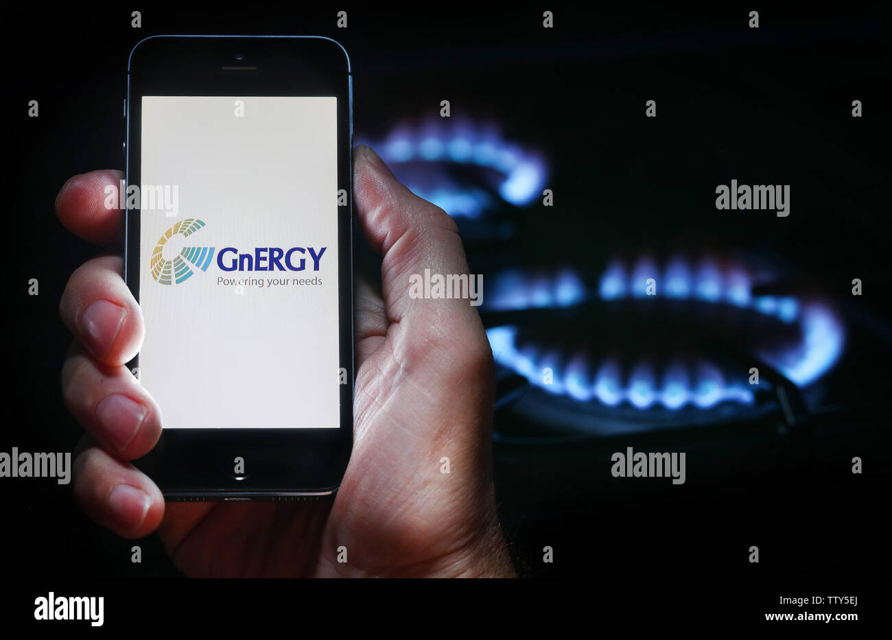 A man looking at the website logo for energy company GnERGY on his phone in front of his gas cooker (editorial use only) Stock Photo