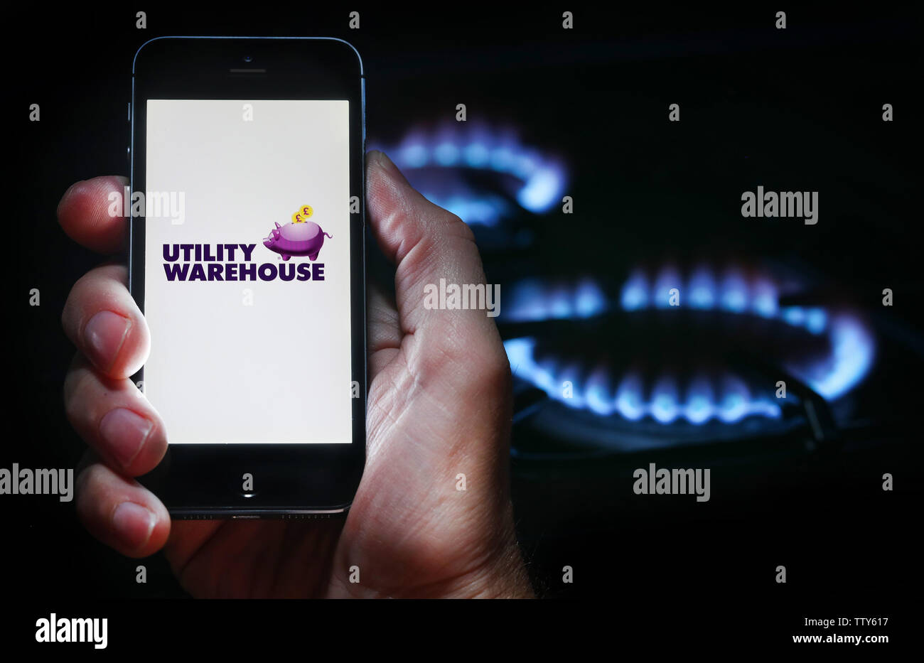 A man looking at the website logo for energy company Utility Warehouse on his phone in front of his gas cooker (editorial use only) Stock Photo