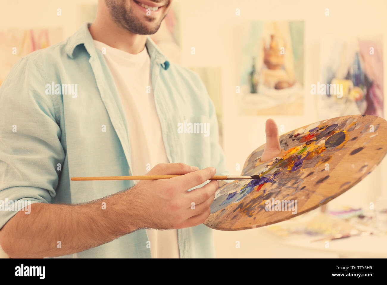 Young male artist with palette and brush in studio, close up Stock