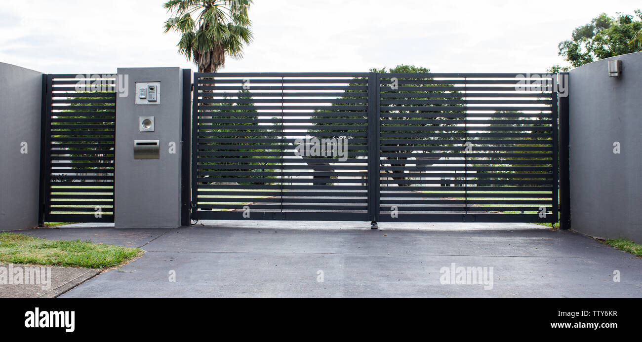 Metal driveway property entrance gates set in concrete fence with