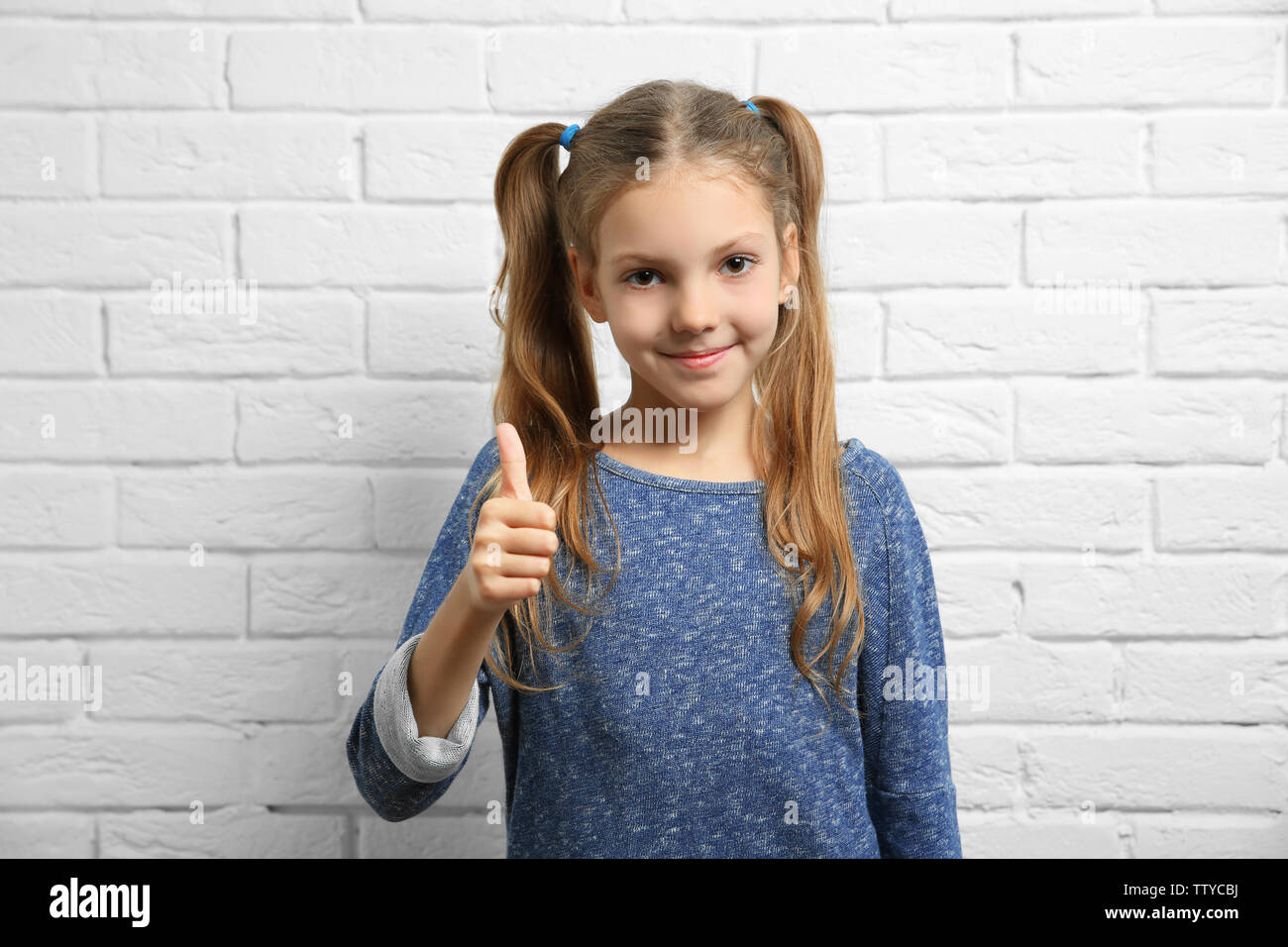 Cute girl showing thumb up sign near brick wall Stock Photo - Alamy