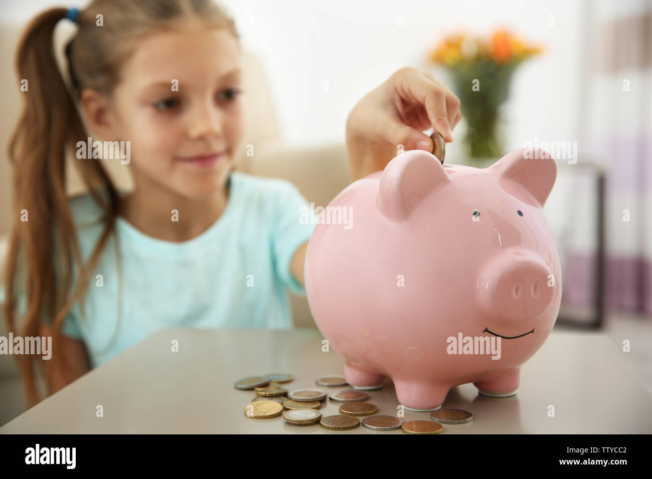 Cute girl putting coins into piggy bank at home Stock Photo - Alamy