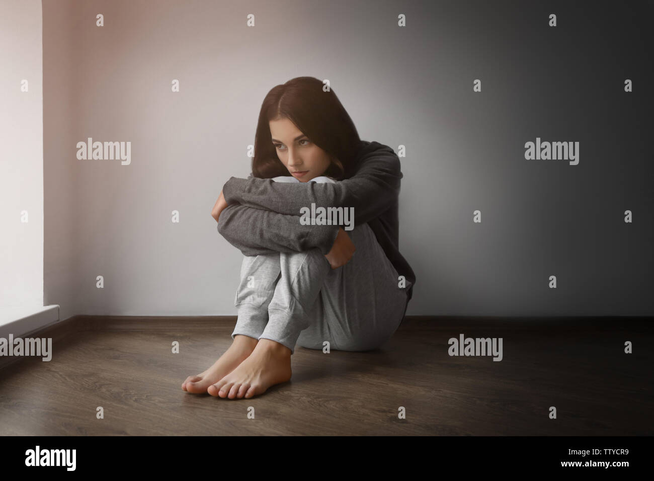 Depressed young woman sitting on floor in empty room Stock Photo - Alamy