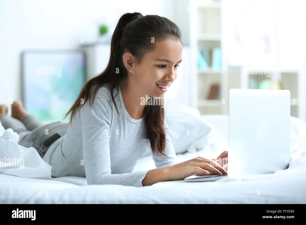 Cute girl lying on bed with laptop Stock Photo - Alamy