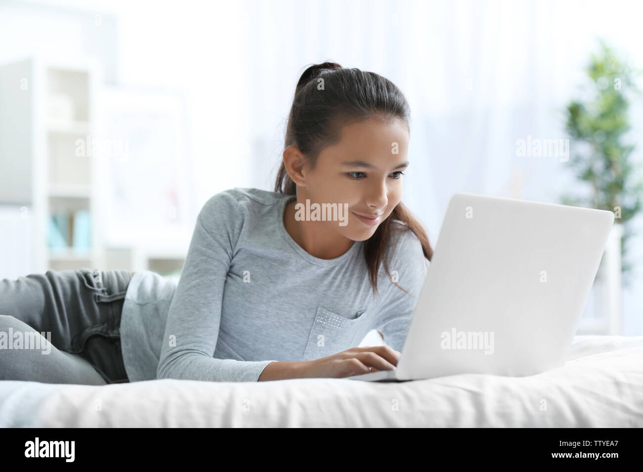 Cute girl lying on bed with laptop Stock Photo - Alamy