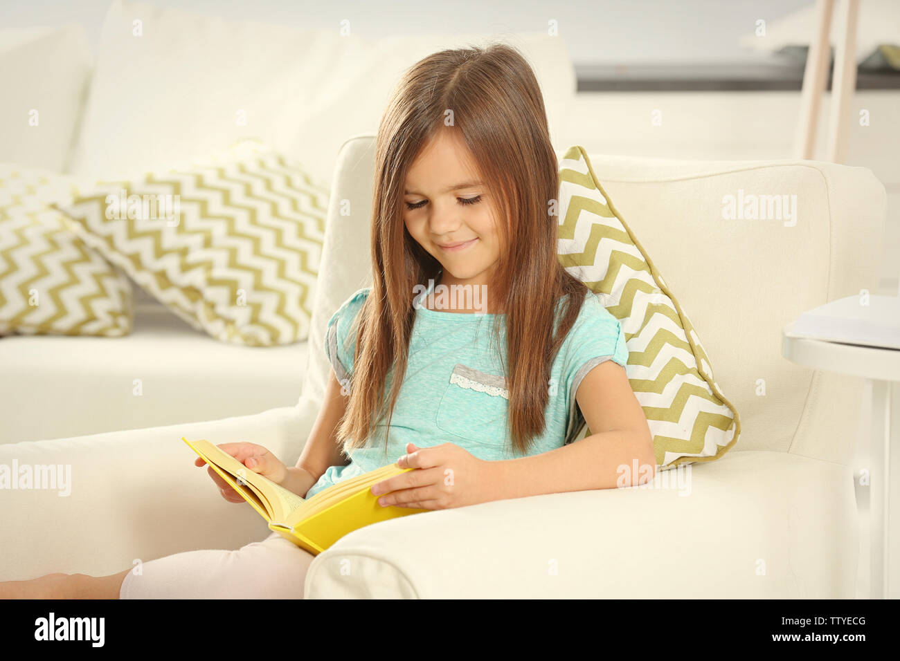 Cute little girl with book sitting on armchair at home Stock Photo - Alamy