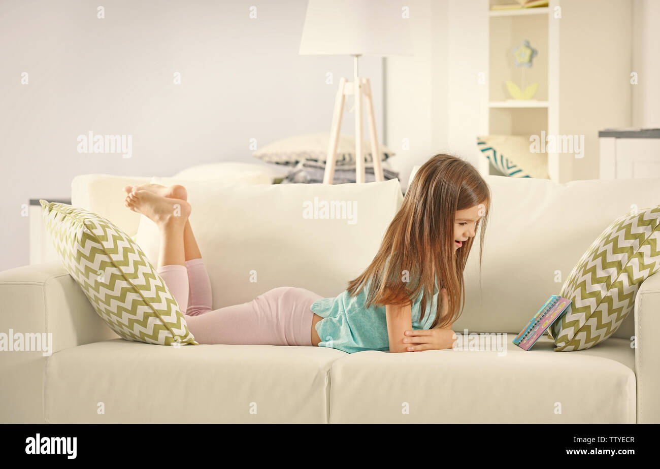 Little girl with book lying on sofa at home Stock Photo Alamy